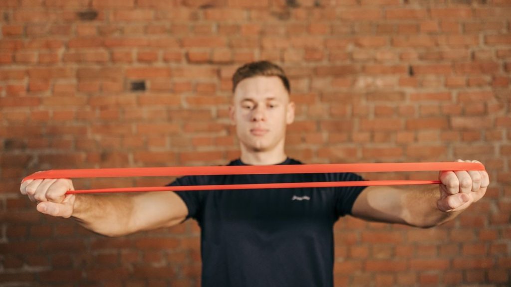 Adult male using a resistance band for fitness training against a brick wall backdrop.